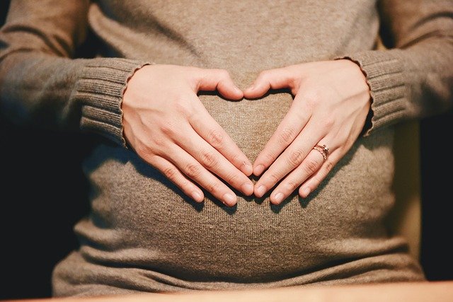hands, forming a heart shape on a pregnant woman's belly
