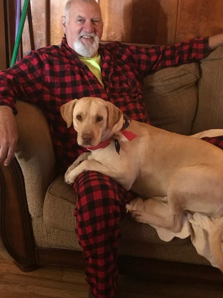 Man in a plaid robe sitting on a couch with a big yellow dog.