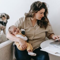 Woman holding a baby sitting at a computer with a small dog looking on