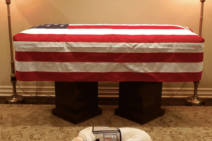 dog lying by a casket with aa flag on it