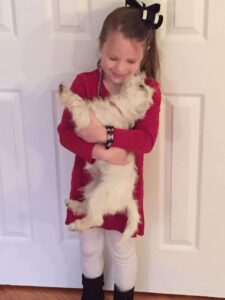 Little girl holding a white dog and loving on her